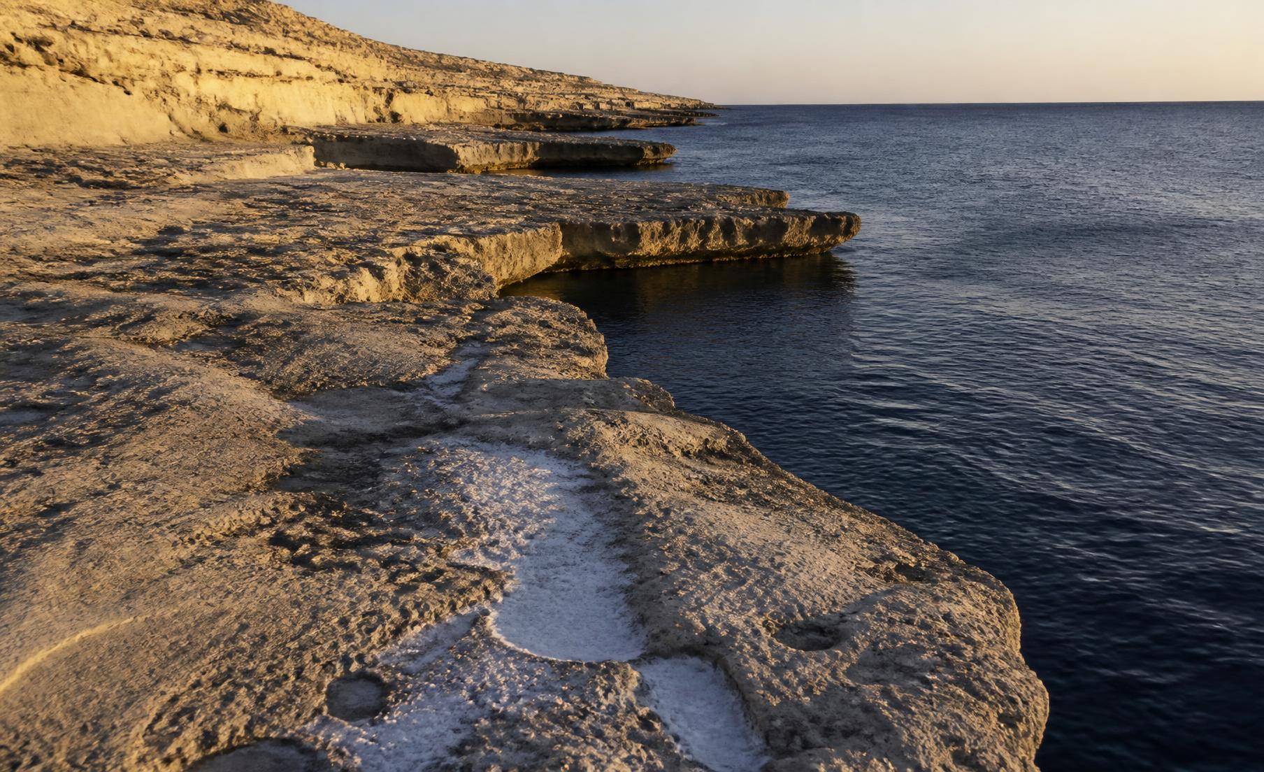 Weathered Maltese limestone shelves meeting deep blue sea in late light